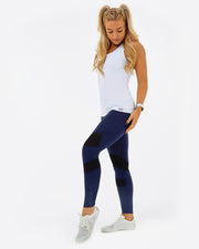 white womens sustainable gym top. White vest ovre navy leggings with mesh design. KAMI branding on the ankle