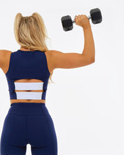 back of a woman lifting weights wearing a navy activewear set, the crop top has white panels on the back