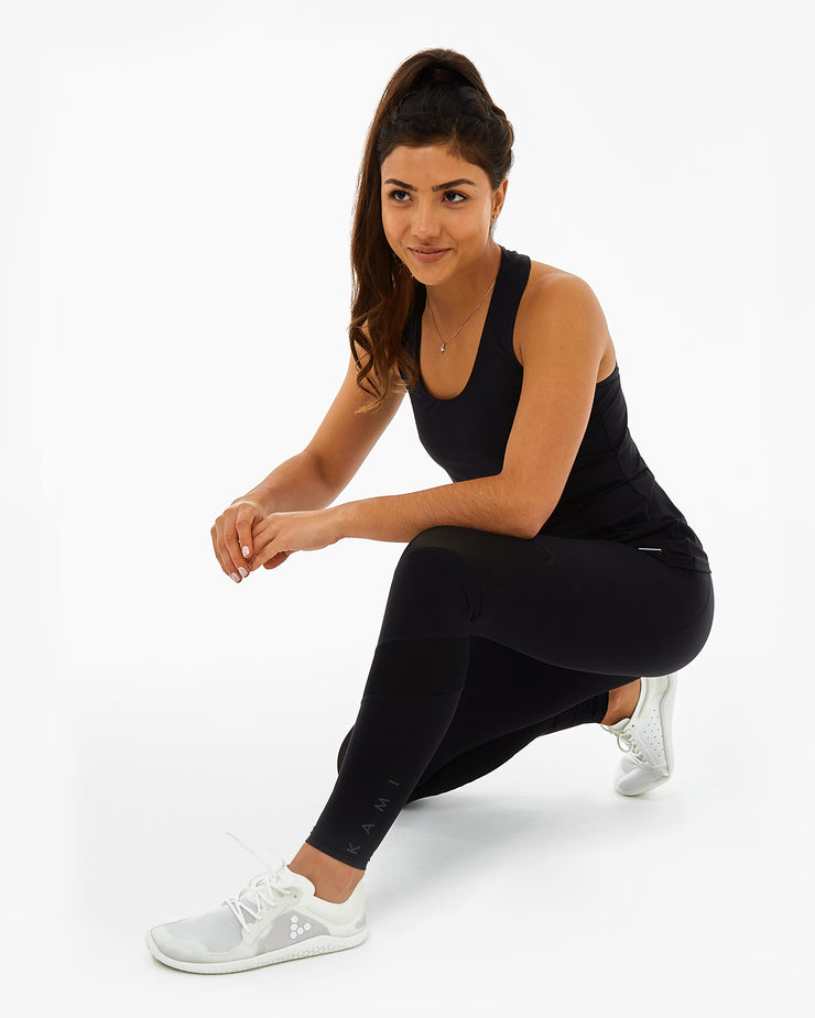 woman crouched on the floor wearing recycled plastic black gym leggings with KAMI branding on the side and a black sustainable gym top