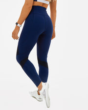 woman in navy gym leggings with black mesh paneling and KAMI branding on the leg. Sustainable activewear made from recycled plastic